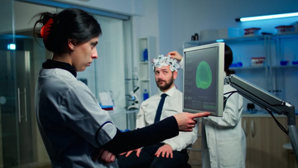 woman-researcher-looking-monitor-analysing-brain-scan-while-coworker-discussing-with-patient-background-about-side-effects (1)